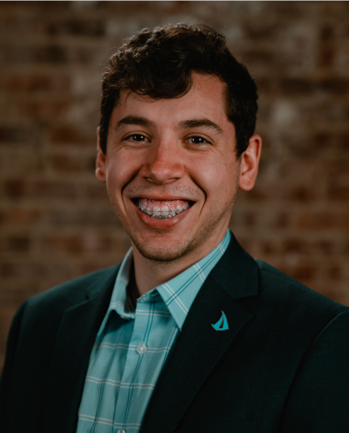 Landon smiles for his headshot in front of a brick wall in the Jacht space
