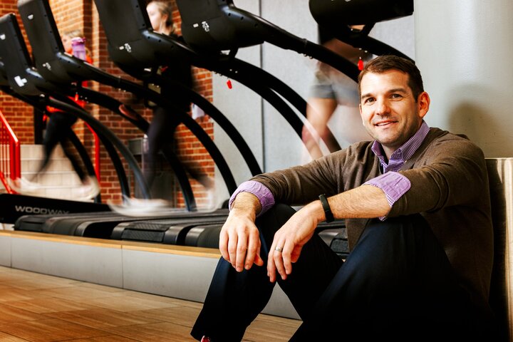 Zac smiles for a photo as students run on the treadmills behind him