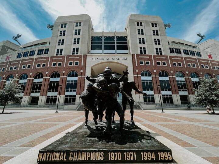The sun shines on the top of a sculpture of football players outside Memorial Stadium
