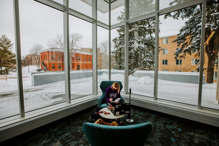 A student writes in a notebook near the windows of Dinsdale Learning Commons