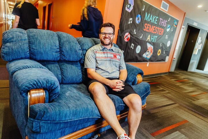 Matt sits on a couch in the hall as students move into the residence hall