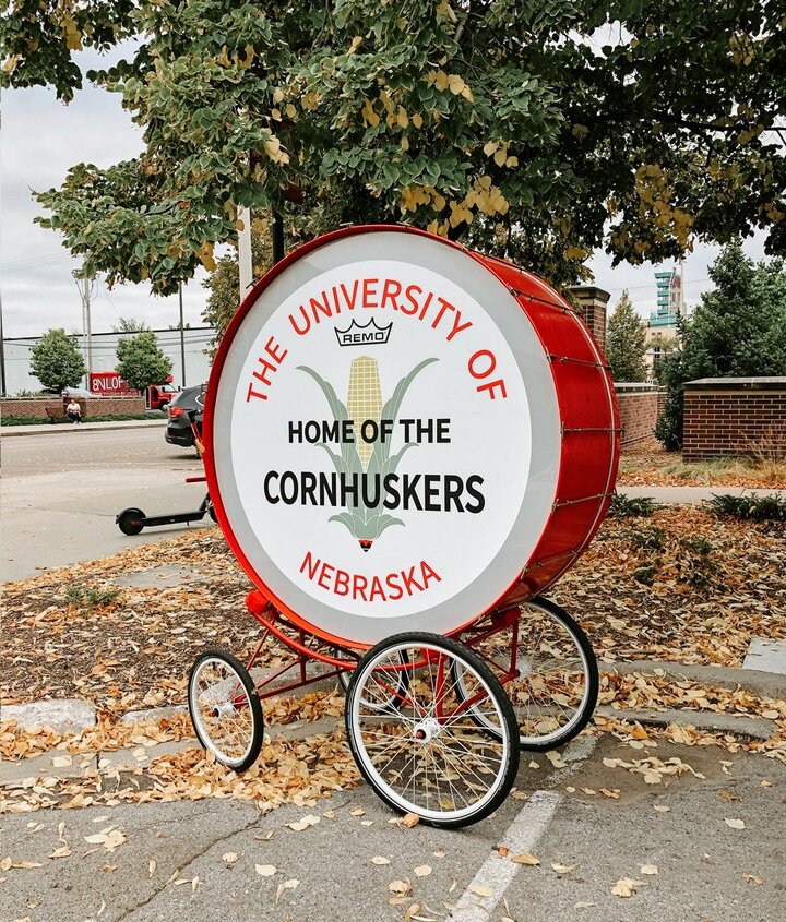 A large red drum with text on the center that says “The University of Nebraska” around the outside and “home of the Cornhuskers” on top of an ear of corn in the center