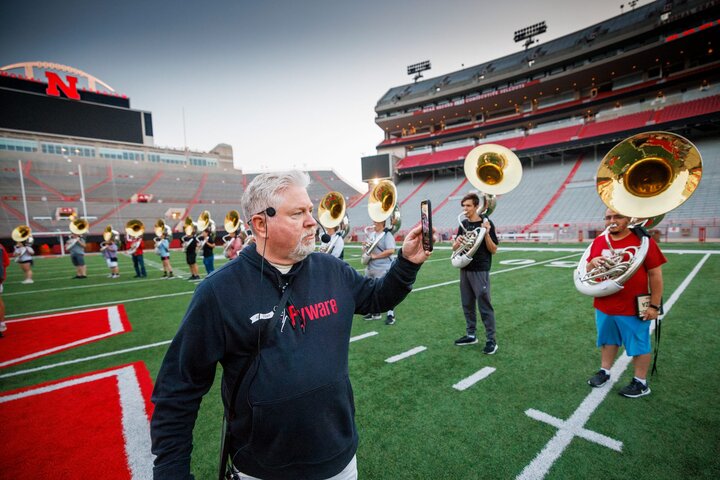 Doug Bush, assistant director of bands, walks through the band as it rehearses while doing a Facebook Live broadcast. Bush said he does the broadcasts on Friday practices and the game-day practice for all the parents and alumni who can’t come to the game.