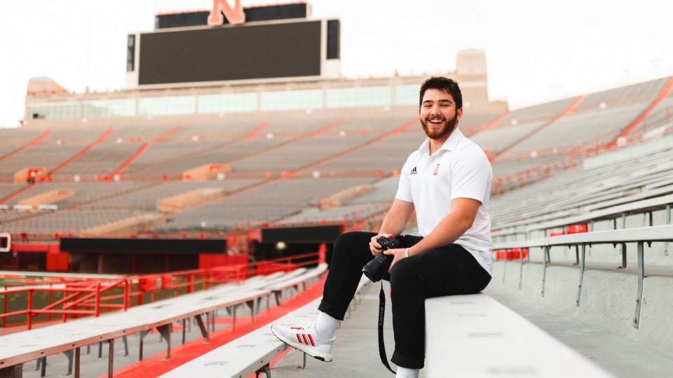 Student holding camera and sitting in stands at Memorial Stadium