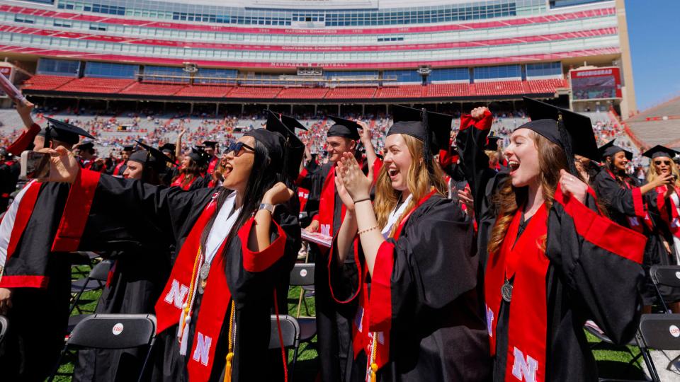 Students smile and wave during commencement at Memorial Stadium
