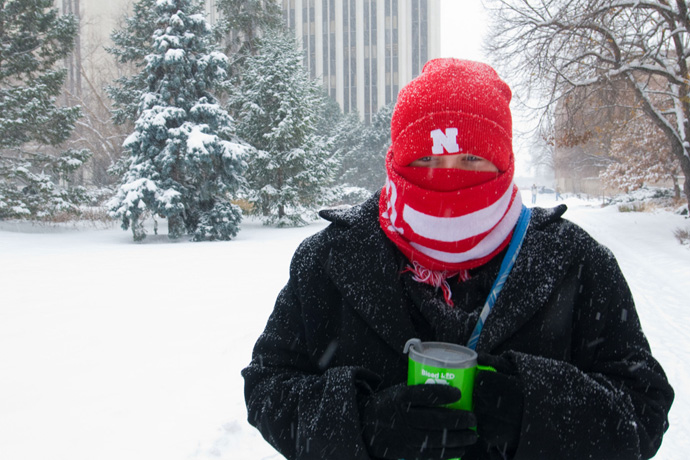 A fully bundled up person outside on campus in a snowshorm with Hamilton and Avery Halls in the backgrond